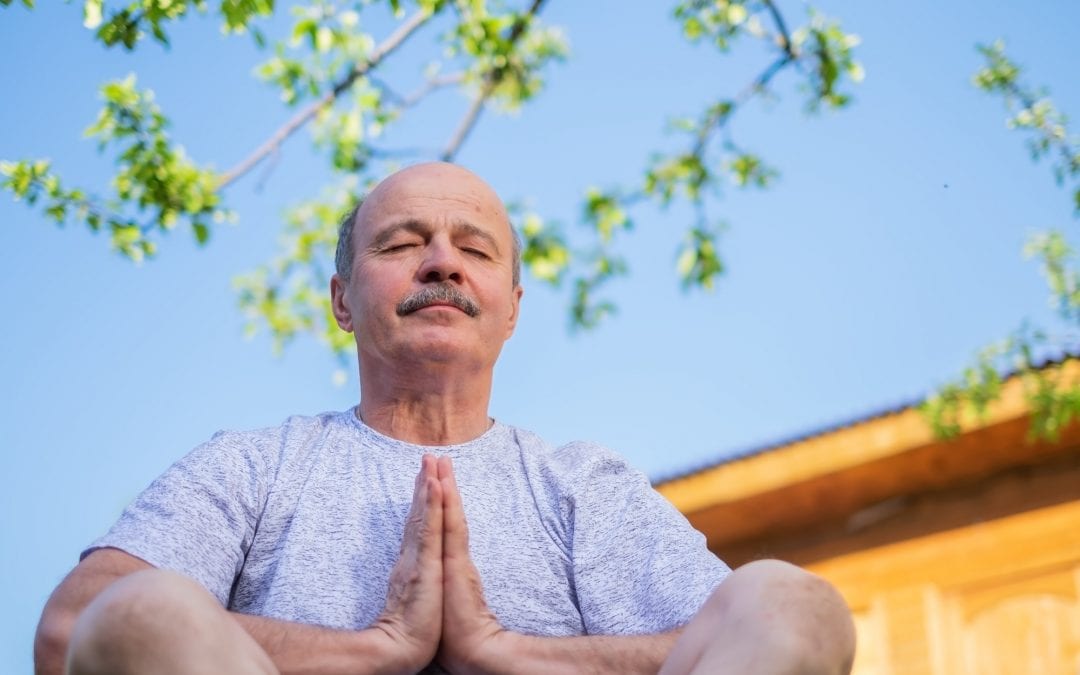 Peaceful senior man meditating seated ooutdoor under the tree. Concept of mental health