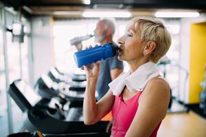 Senior woman drinking bottle of water on threadmill in gym
